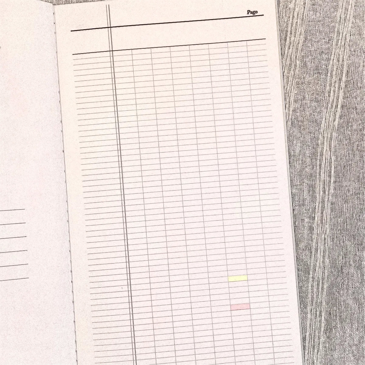 An open notebook or planner showing a lined page with a grid layout, photographed from above on a gray wood-textured surface.