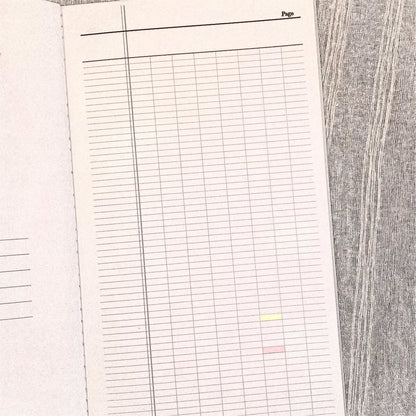 An open notebook or planner showing a lined page with a grid layout, photographed from above on a gray wood-textured surface.