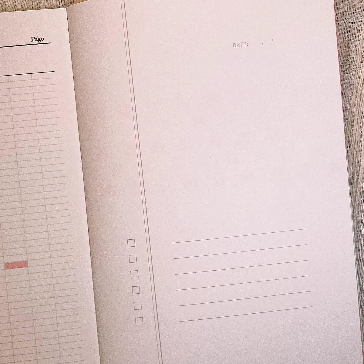 An open notebook or planner showing blank interior pages with lined writing areas, checkboxes, and a page number column, photographed on a light wood surface.