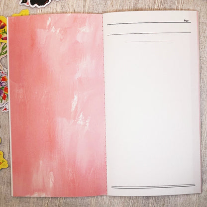 An open notebook or journal showing a textured pink left page and a blank white right page with thin black lines and the word 'Page' at the top right, photographed from above on a light wood surface.